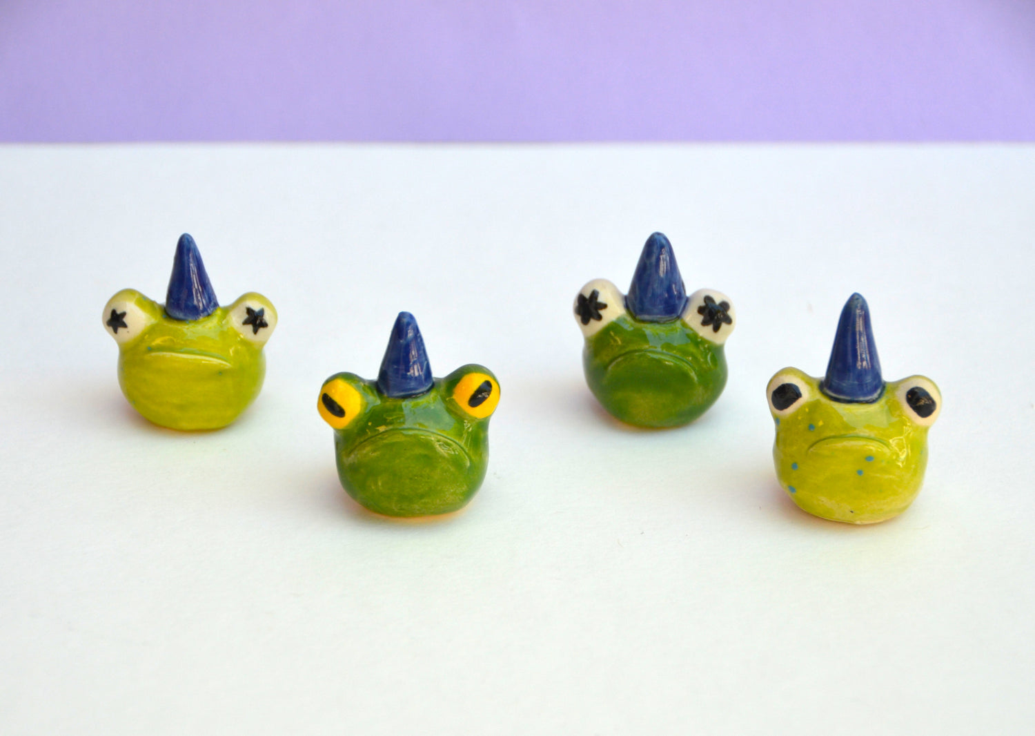 4 miniature frog heads all wearing dark blue wizard hats. Each frog has a different eye and pupil design.