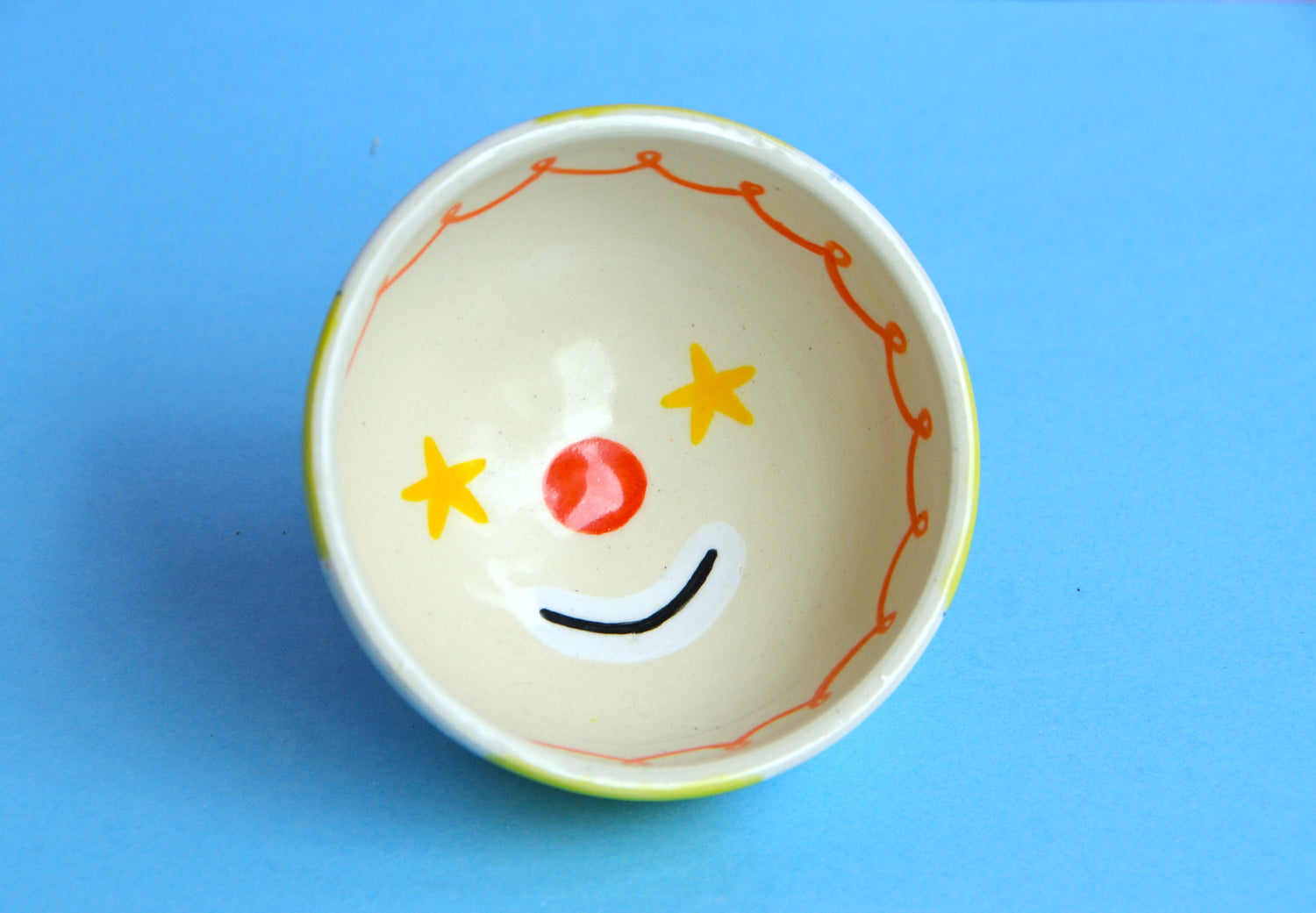 Ceramic bowl woth a starry eyed clown face design on a blue background 